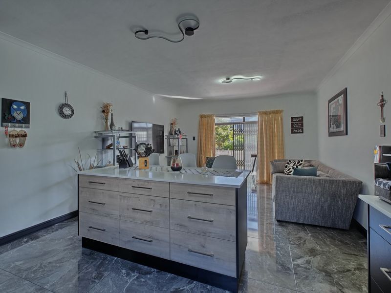 Open-plan living area featuring a modern kitchen island with wood-finish cabinetry, marble-look tiled flooring, and direct access to an outdoor patio area.