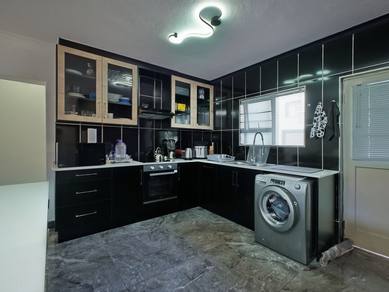 Modern kitchen featuring black cabinetry, contrasting light wood-framed glass cabinets, black tiled walls, stone-look flooring, and integrated appliances.