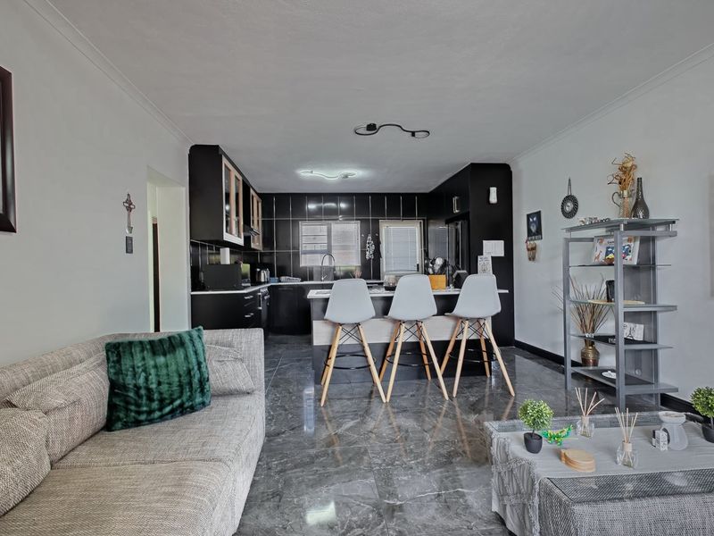 An open-plan living and kitchen area featuring modern black cabinetry, a central kitchen island, and polished marble-look floor tiles throughout.