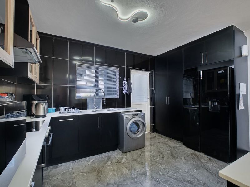 Modern kitchen featuring sleek black cabinetry, contrasting white countertops, black tiled walls, and polished marble-look flooring with integrated appliances.