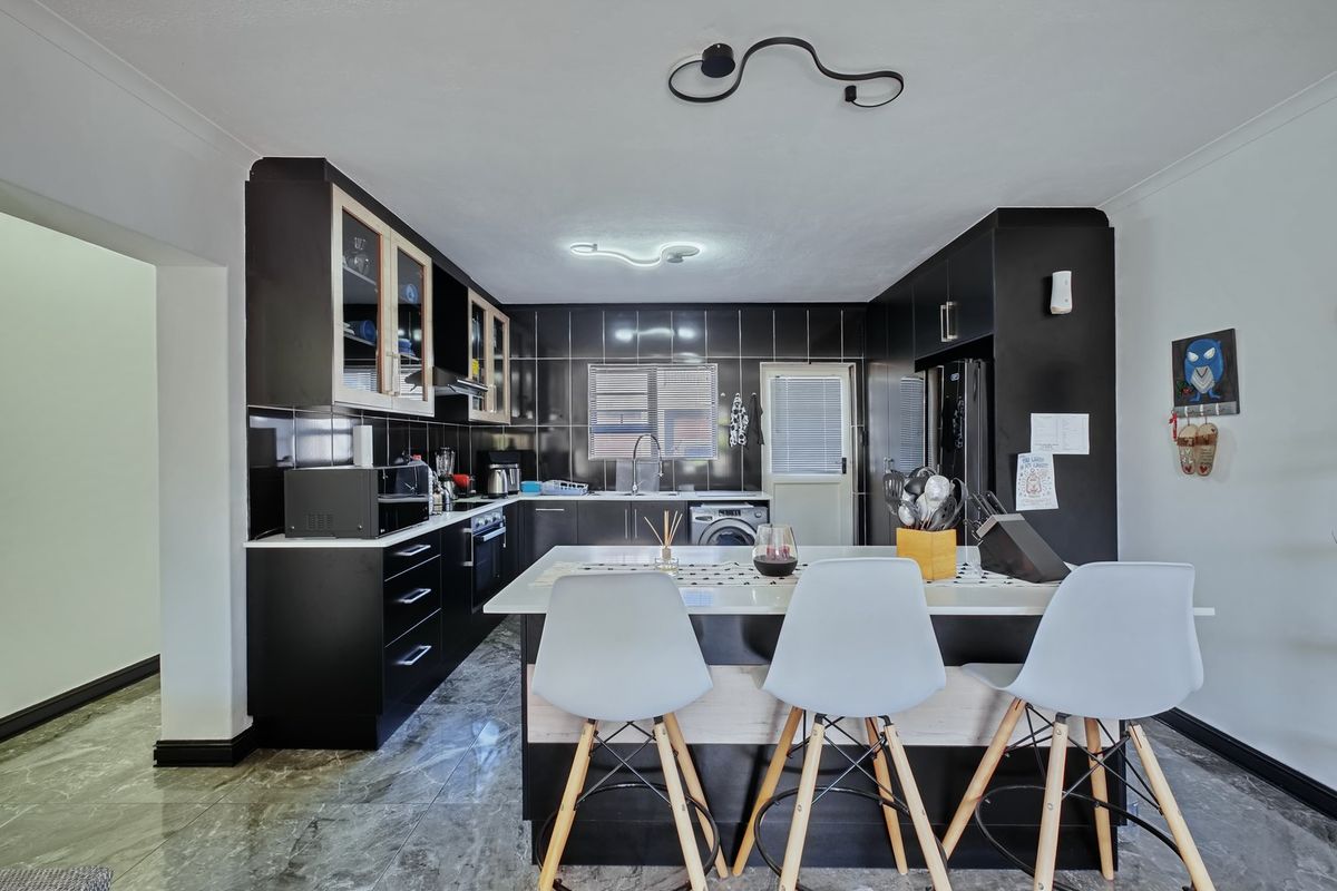 Modern kitchen featuring sleek black cabinetry, stone countertops, a central island, and integrated appliances with high-contrast tiled finishes.