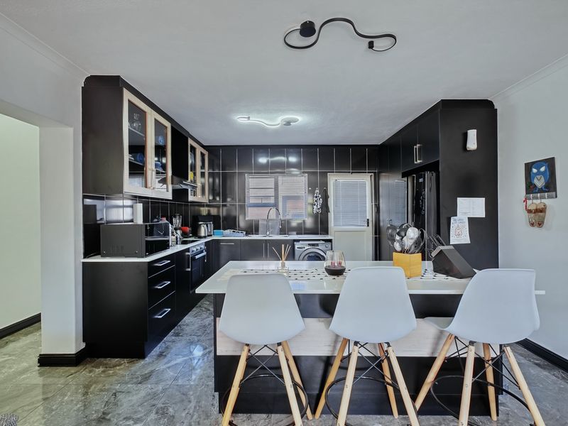 Modern kitchen featuring sleek black cabinetry, stone countertops, a central island, and integrated appliances with high-contrast tiled finishes.