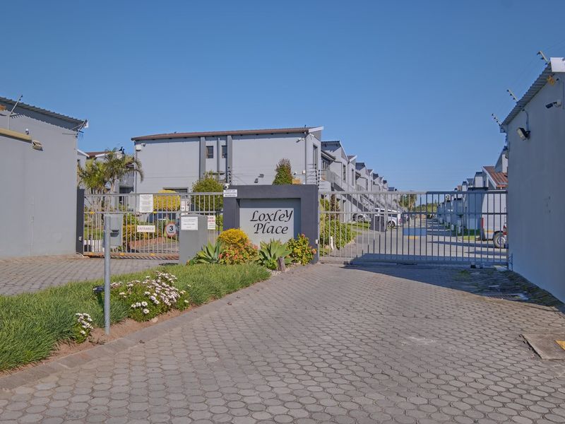 The secure entrance to Loxley Place apartment complex, featuring a paved driveway, automated security gate, and perimeter electric fencing.