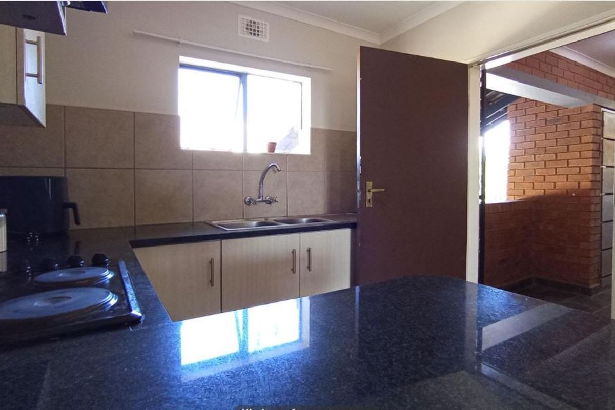 A functional kitchen featuring granite countertops, built-in cabinetry, a double sink, and an electric hob, with direct access to an adjacent outdoor area.