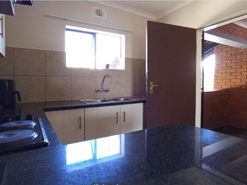 A functional kitchen featuring granite countertops, built-in cabinetry, a double sink, and an electric hob, with direct access to an adjacent outdoor area.