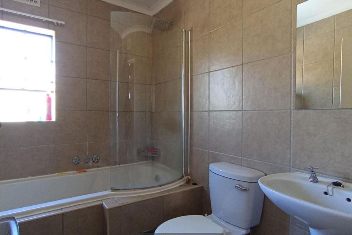 A functional bathroom featuring a bathtub with a glass shower screen, pedestal basin, and neutral wall tiling.