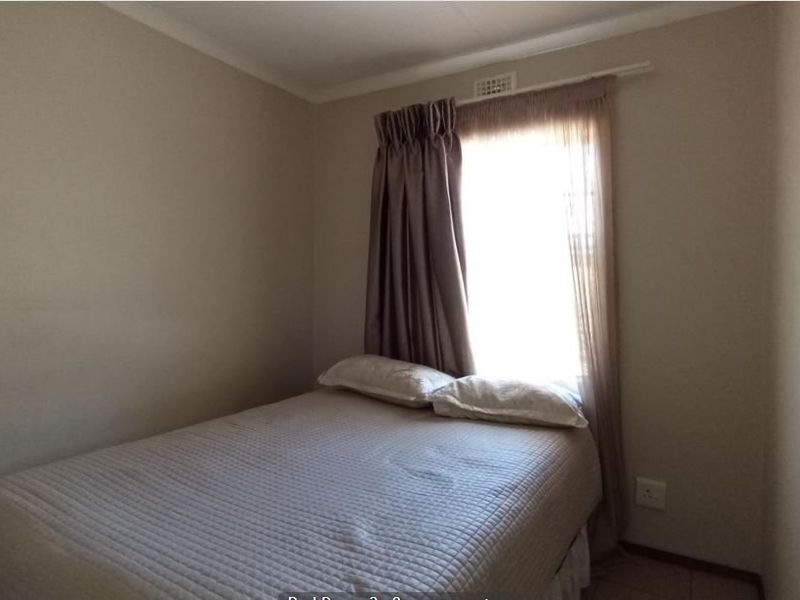 A standard bedroom featuring neutral wall finishes, a window with curtain rail, and basic electrical infrastructure.