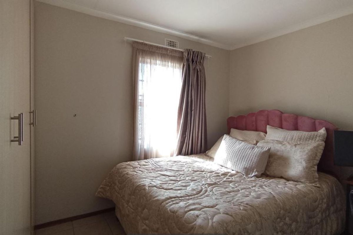 A functional bedroom featuring neutral wall tones, tiled flooring, and a built-in wardrobe for storage.