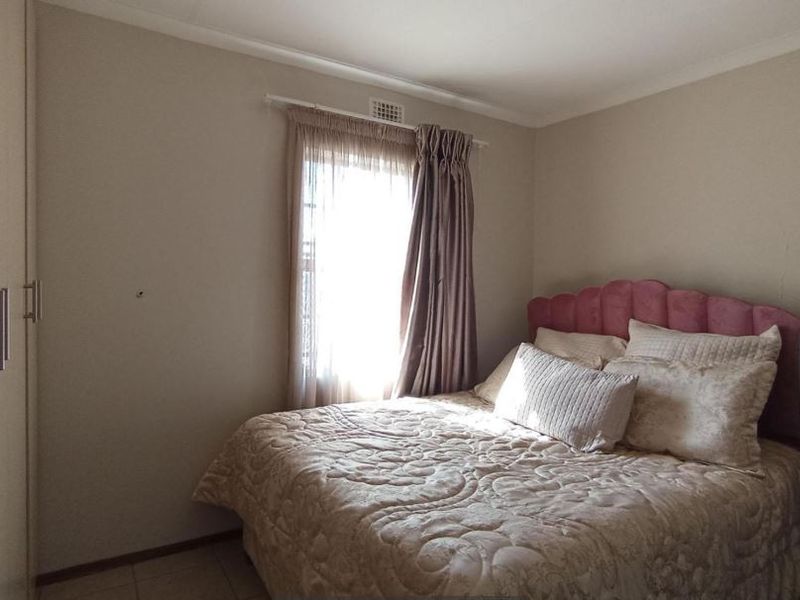 A functional bedroom featuring neutral wall tones, tiled flooring, and a built-in wardrobe for storage.