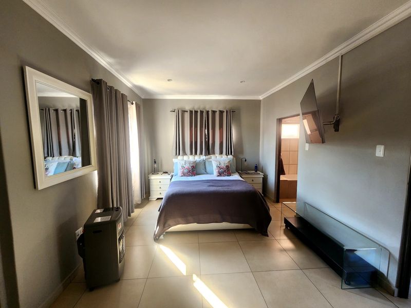 A well-maintained bedroom featuring neutral tiled flooring, crown molding, recessed lighting, and direct access to an en-suite bathroom.