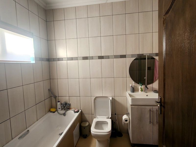 A functional bathroom featuring a bathtub, toilet, and vanity cabinet with a washbasin, finished with neutral wall and floor tiling.