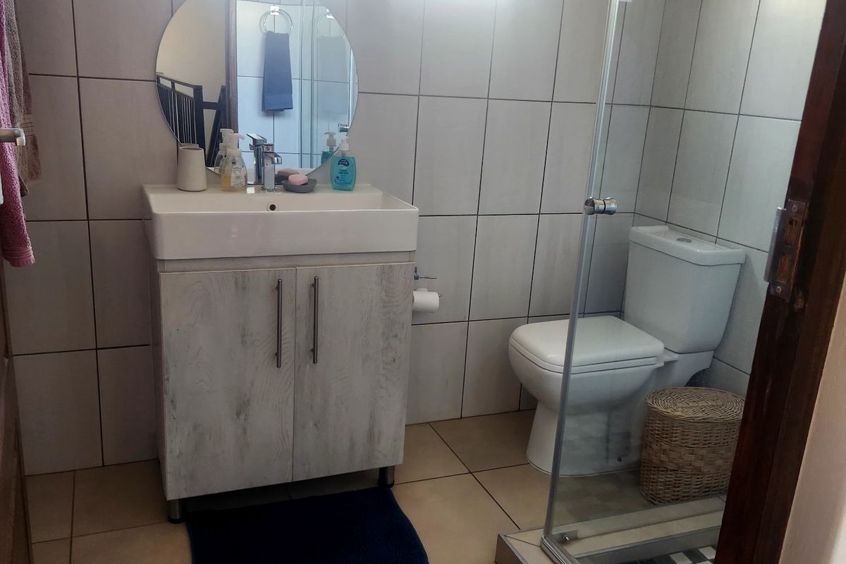 A functional bathroom featuring a vanity cabinet with basin, a toilet, and a glass-enclosed shower with tiled finishes throughout.