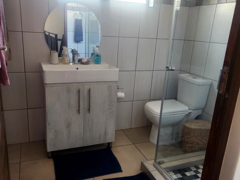 A functional bathroom featuring a vanity cabinet with basin, a toilet, and a glass-enclosed shower with tiled finishes throughout.