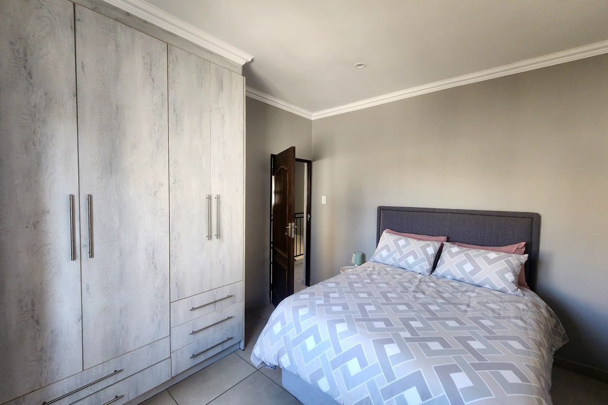 A well-maintained bedroom featuring neutral grey walls, large built-in cupboards with a wood-grain finish, tiled flooring, and modern recessed lighting.