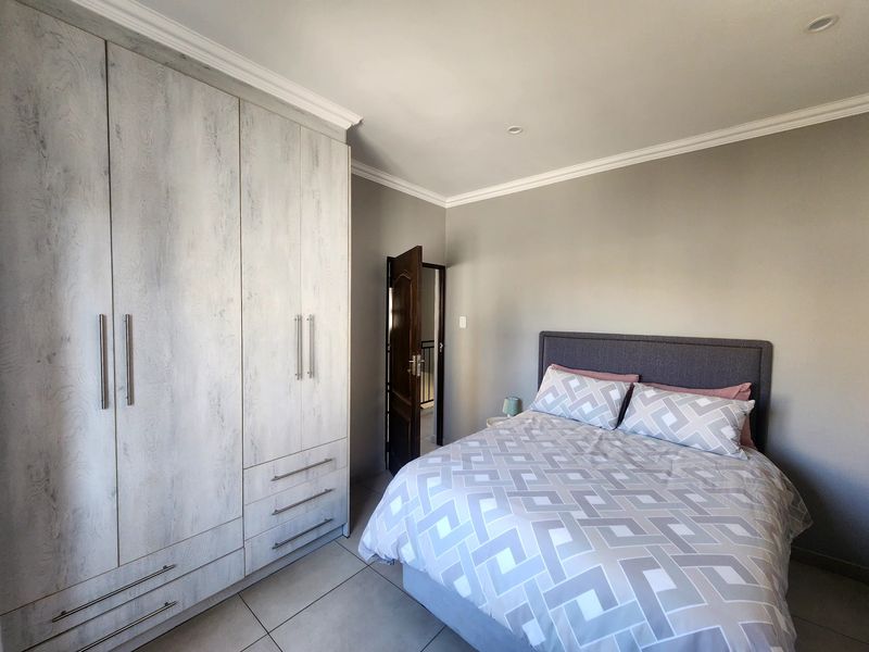 A well-maintained bedroom featuring neutral grey walls, large built-in cupboards with a wood-grain finish, tiled flooring, and modern recessed lighting.