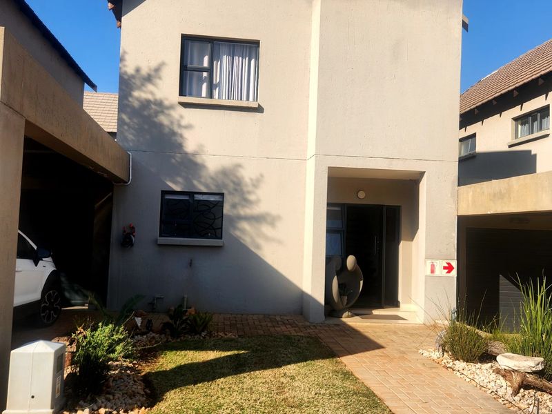 Front elevation of a two-story townhouse featuring a paved walkway, small garden, and integrated carport area.