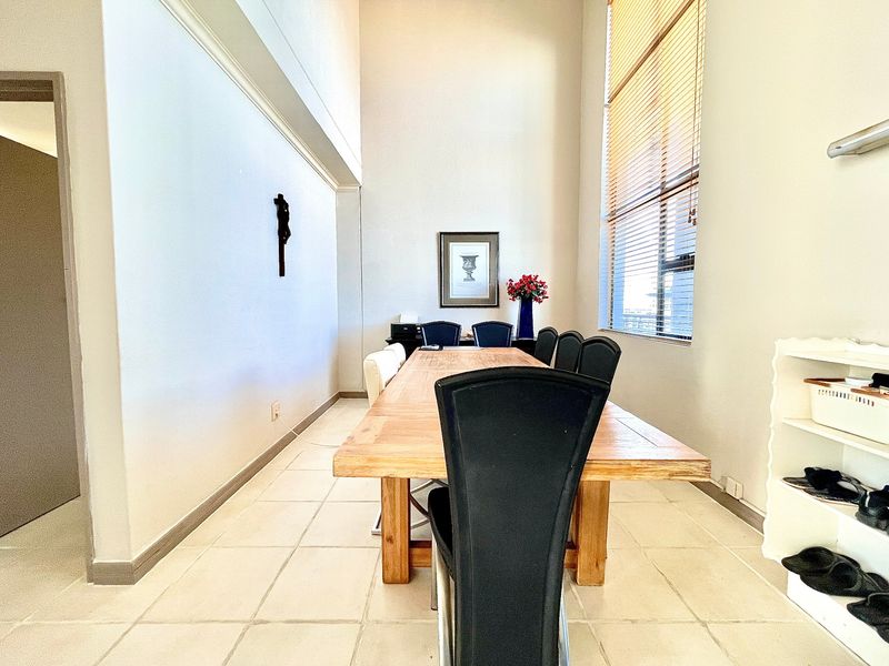 Spacious dining area featuring high ceilings, large windows with venetian blinds, and neutral tiled flooring, offering a bright and airy atmosphere.