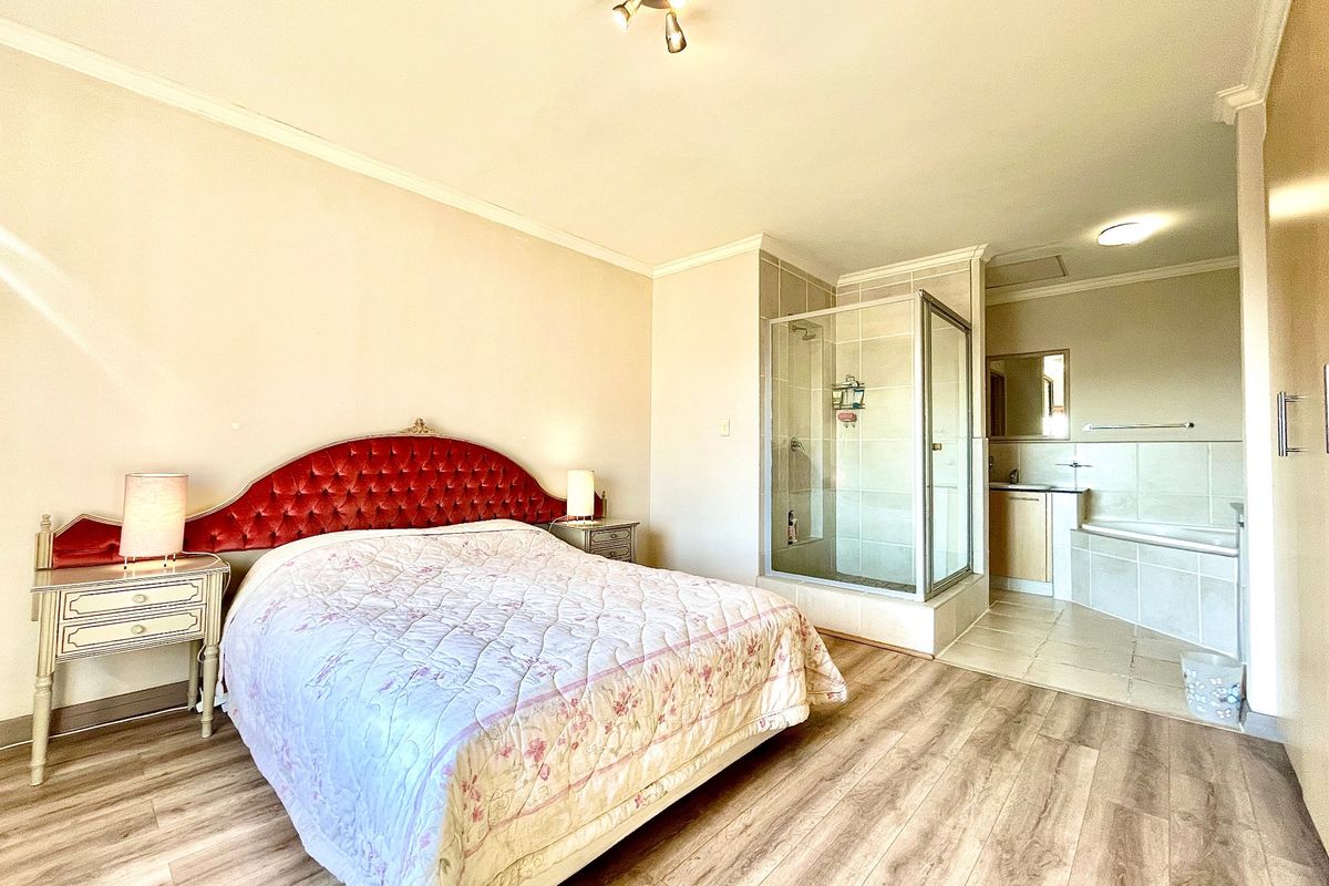 Spacious bedroom featuring laminate flooring and an open-plan en-suite bathroom with a glass-enclosed shower, built-in bathtub, and vanity basin.
