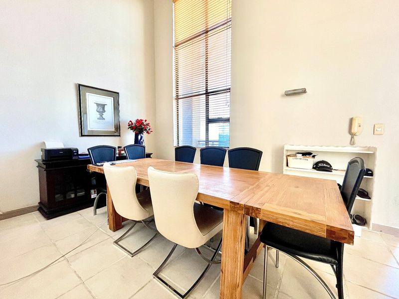A bright dining area featuring high ceilings, large windows with venetian blinds, and neutral tiled flooring, creating a spacious and well-lit atmosphere.