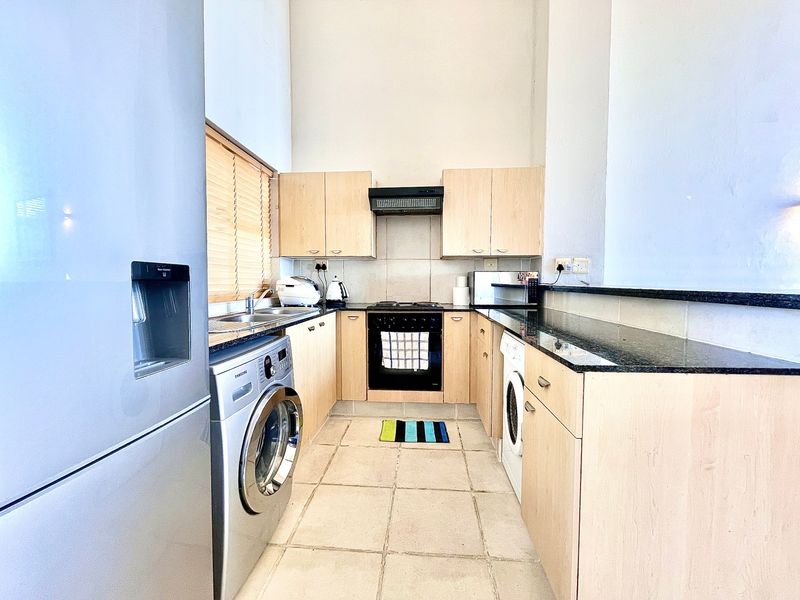 Functional kitchen featuring light wood cabinetry, granite countertops, integrated appliances, and tiled flooring, offering a practical layout for daily cooking and laundry needs.