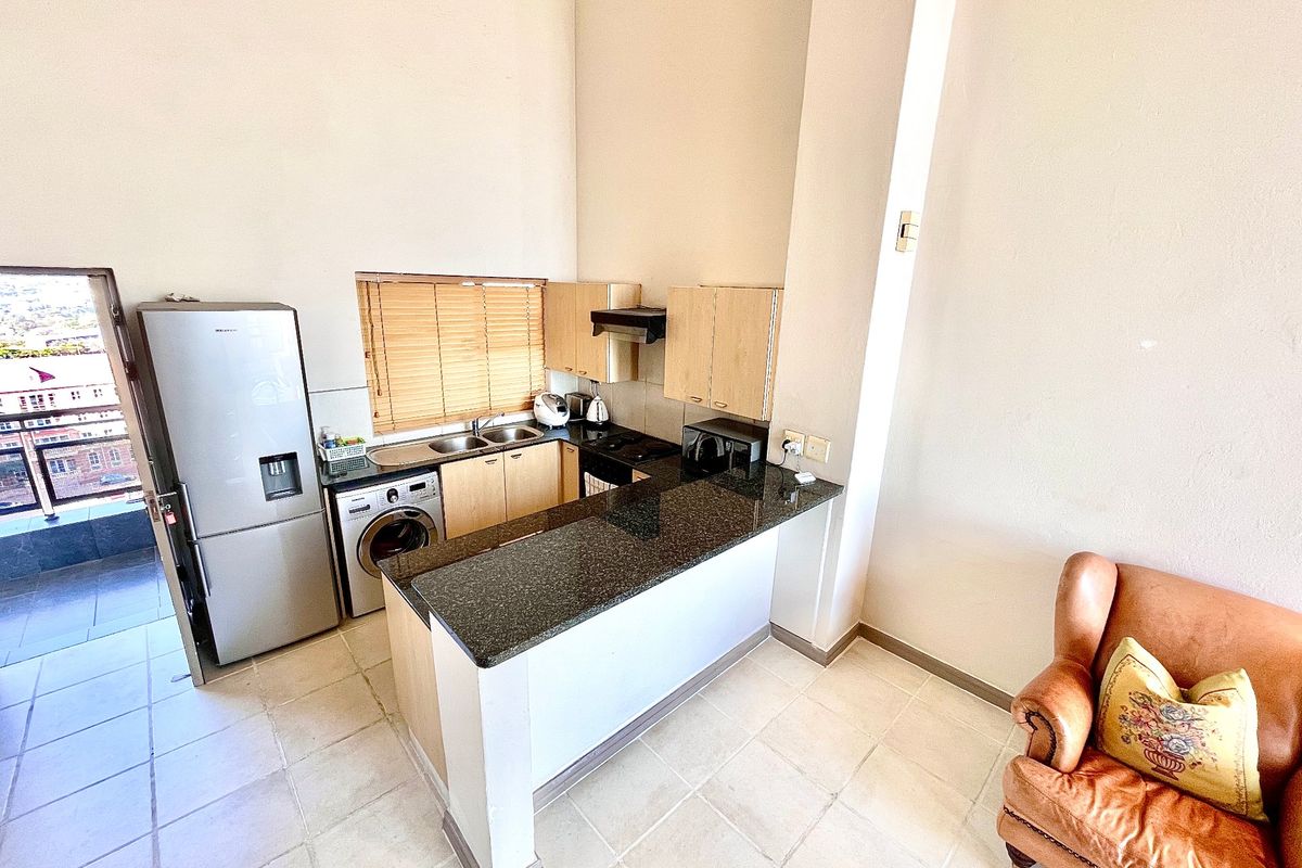 Compact kitchen featuring granite countertops, built-in cabinetry, a double sink, and an integrated hob with extractor fan, opening onto a tiled living area.
