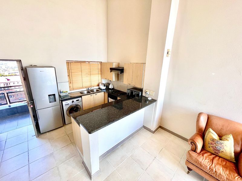 Compact kitchen featuring granite countertops, built-in cabinetry, a double sink, and an integrated hob with extractor fan, opening onto a tiled living area.