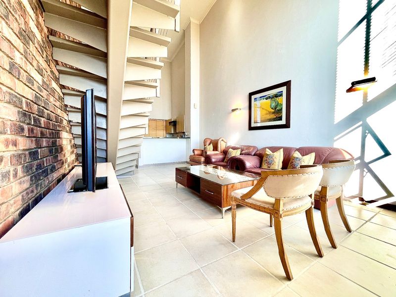 Spacious double volume living area featuring an exposed brick feature wall, tiled flooring, and a prominent spiral staircase leading to the upper level.