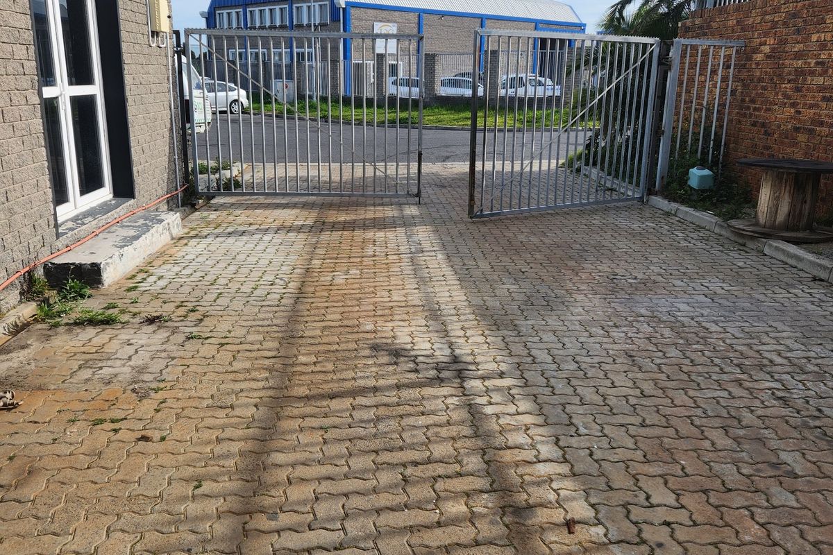 Commercial property entrance featuring a paved driveway, secure metal gates, and brick boundary walling.