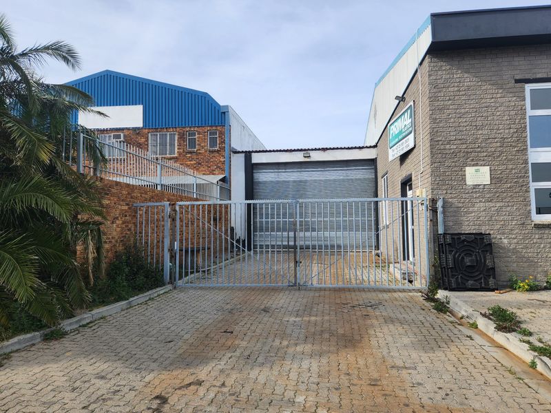 Commercial property entrance featuring a paved driveway, secure metal gate, and a roller shutter door access point.