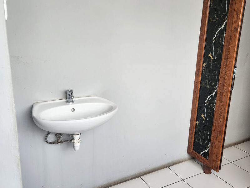 A minimalist bathroom space featuring a wall-mounted basin, white ceramic floor tiles, and a decorative wood-framed accent panel.