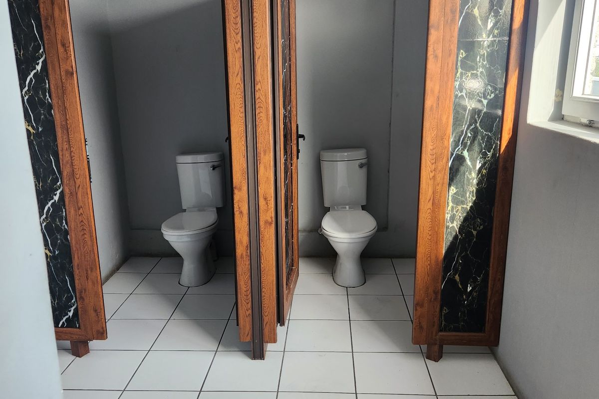 A commercial bathroom facility featuring two individual toilet stalls with wooden frames and decorative marble-effect panels, finished with white floor tiles.