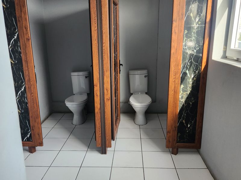 A commercial bathroom facility featuring two individual toilet stalls with wooden frames and decorative marble-effect panels, finished with white floor tiles.