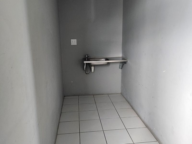 A compact, empty utility or scullery area featuring tiled flooring and a wall-mounted stainless steel sink.