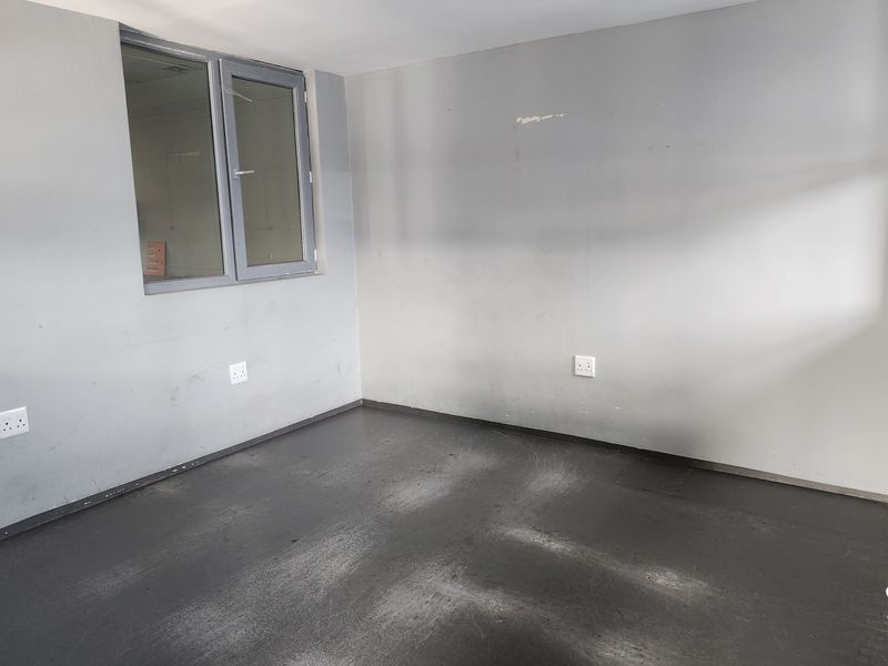 An empty commercial office space featuring grey painted walls, dark flooring, and an aluminium-framed window, suitable for a professional workspace setup.