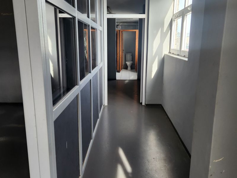 A commercial hallway featuring aluminium framed glass partitions and access to a restroom, showing signs of wear on the walls and flooring.