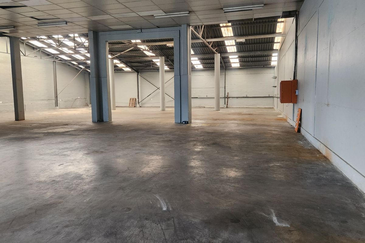 Spacious industrial warehouse or utility space featuring concrete flooring, exposed steel structural columns, skylights, and functional overhead lighting.