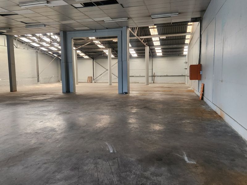 Spacious industrial warehouse or utility space featuring concrete flooring, exposed steel structural columns, skylights, and functional overhead lighting.