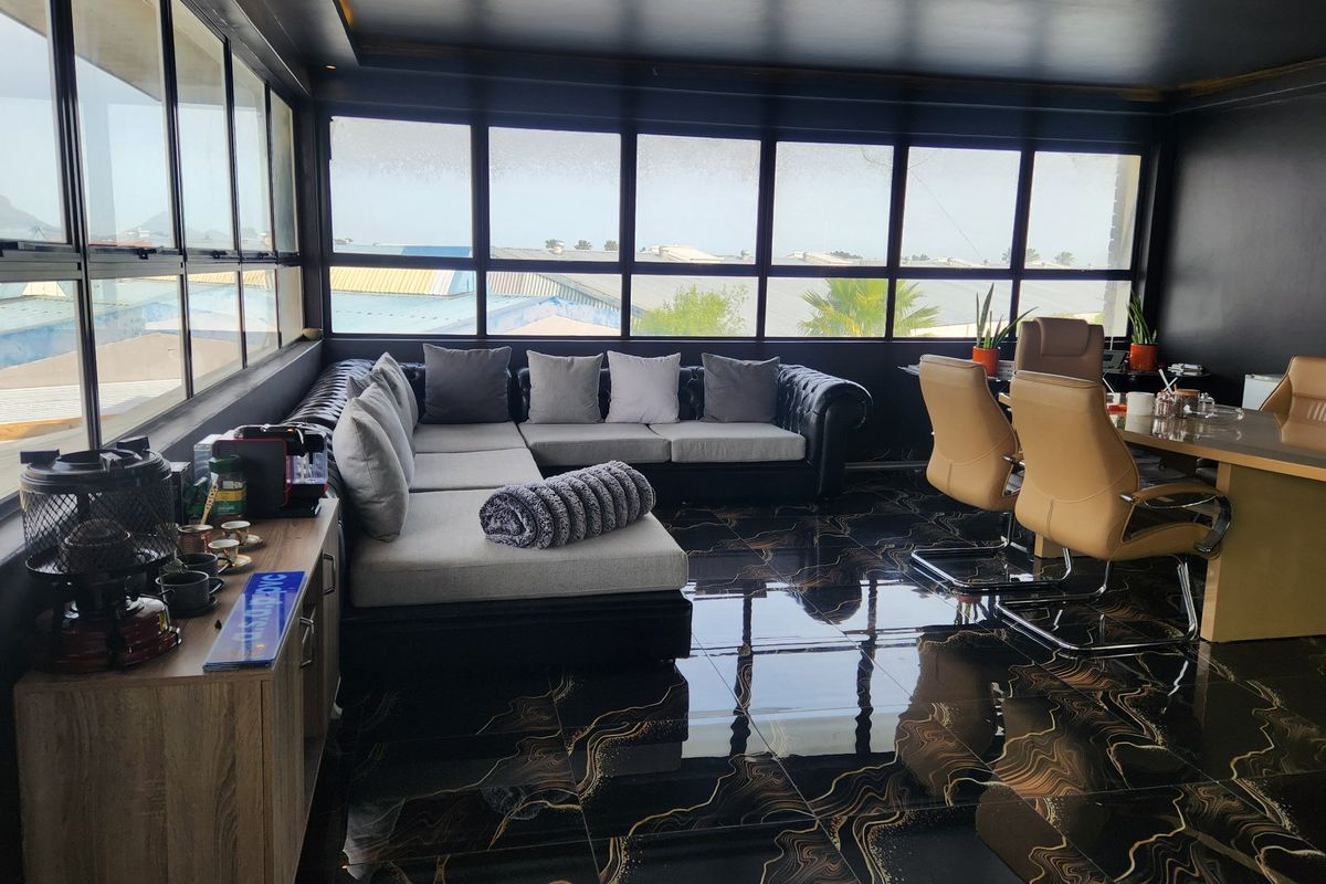 A modern office space featuring high-gloss patterned floor tiles, dark walls, and expansive windows providing ample natural light and an elevated view.