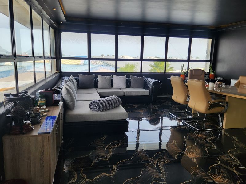 A modern office space featuring high-gloss patterned floor tiles, dark walls, and expansive windows providing ample natural light and an elevated view.