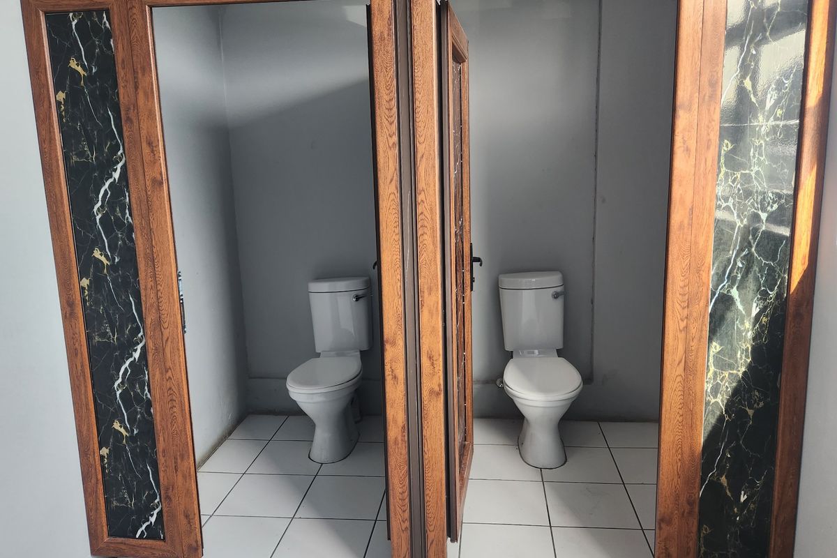 Commercial bathroom facility featuring two separate toilet cubicles with wood-look frames and decorative marble-effect panels.