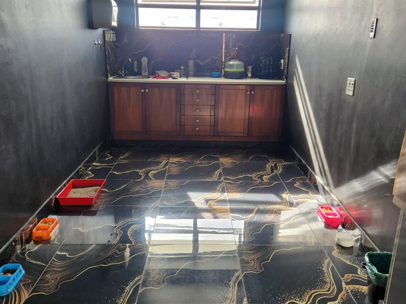 A functional scullery or utility area featuring dark decorative floor tiles, built-in wooden cabinetry, a sink, and a rear window for natural light.