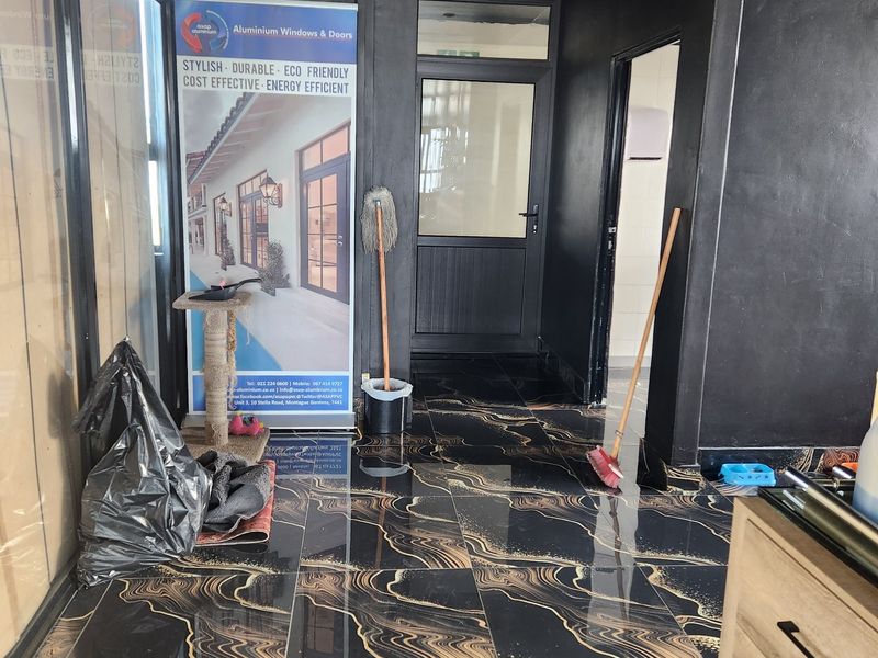 A modern commercial hallway featuring striking black and gold patterned floor tiles and dark painted walls with aluminium framed glass door access.