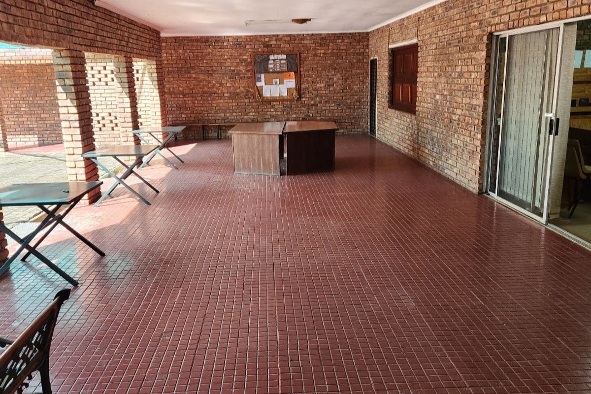 A spacious covered patio featuring exposed brick walls, tiled flooring, and brick pillars, offering a versatile outdoor entertainment area.