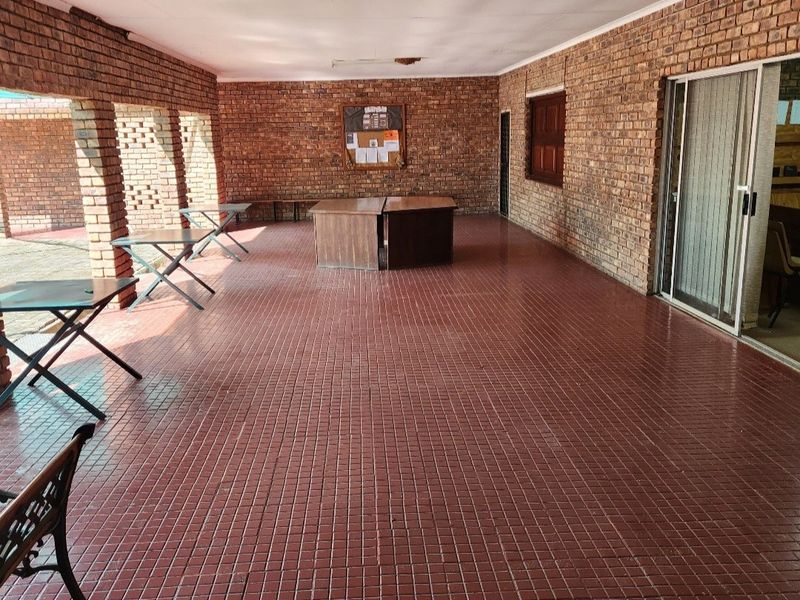 A spacious covered patio featuring exposed brick walls, tiled flooring, and brick pillars, offering a versatile outdoor entertainment area.