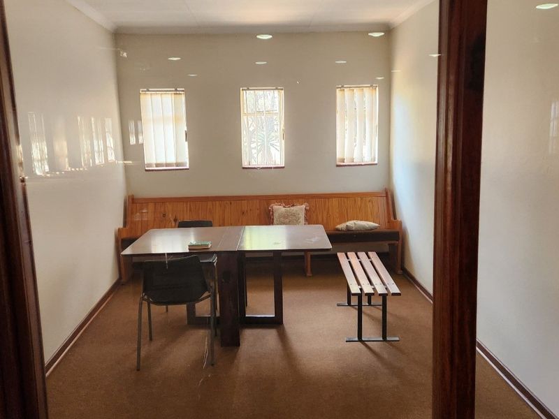 A functional office space featuring a built-in wooden bench, vertical blinds, and recessed lighting, providing a simple and practical work environment.