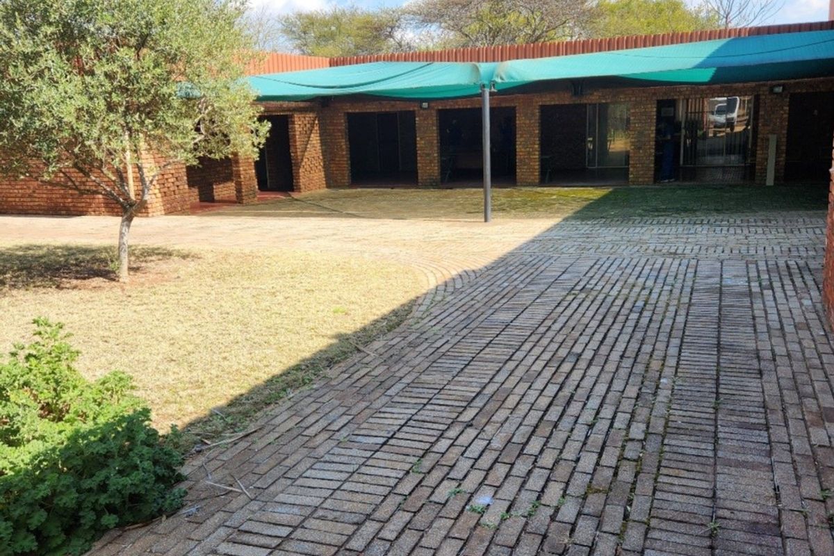 Rear exterior view of the farm property featuring a brick-paved courtyard, covered walkway with shade cloth, and established garden area.