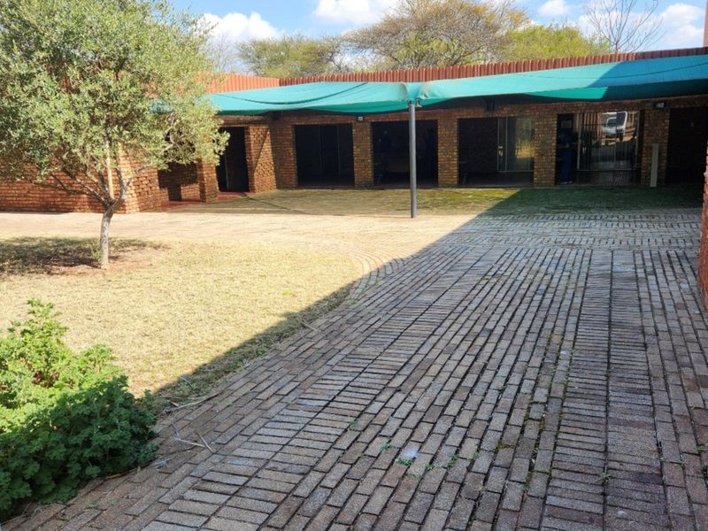 Rear exterior view of the farm property featuring a brick-paved courtyard, covered walkway with shade cloth, and established garden area.