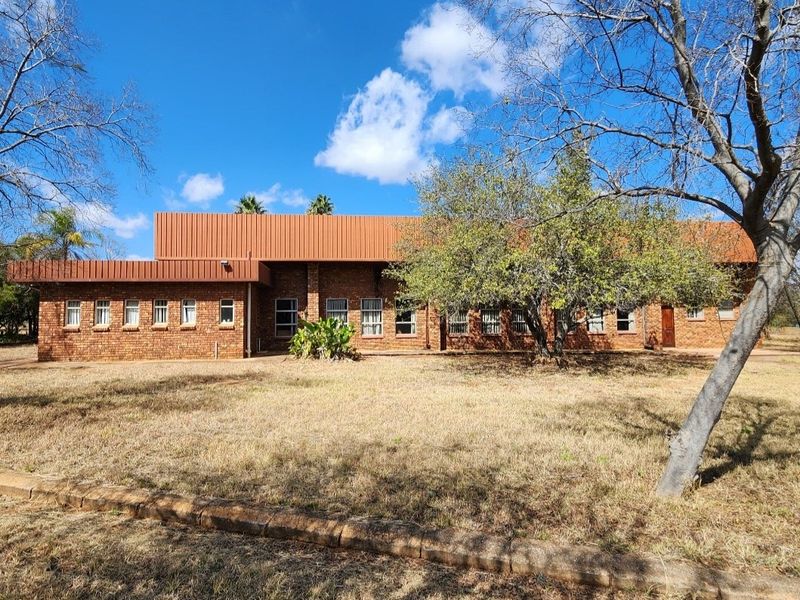 A view of the rear elevation of a face brick farm building featuring a prominent metal roof and multiple casement windows set in a rural landscape.