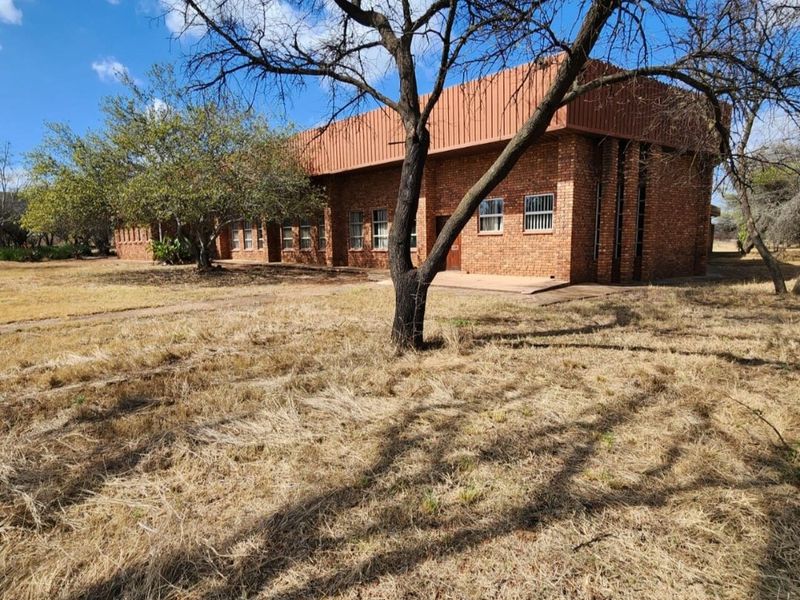 A view of the rear face brick farm building featuring a metal roof and security-fitted windows set within a large, dry grass landscape.
