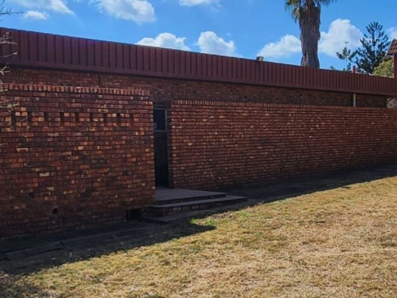 Rear view of a face brick farm building featuring a distinctive bell tower and surrounding dry landscape.